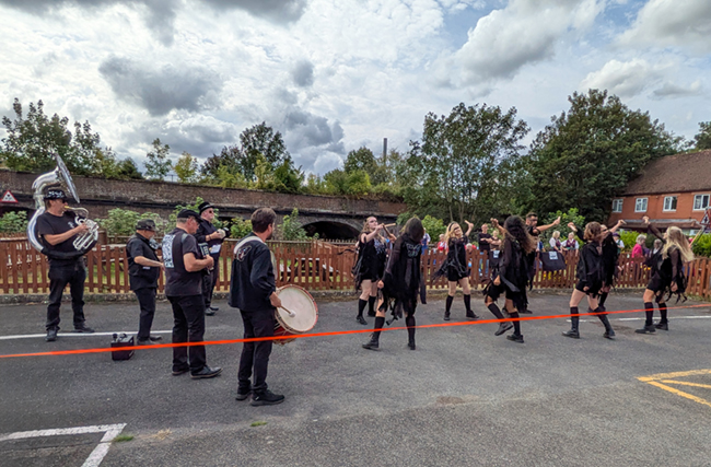 Erstwhile Morris Dancers and musicians in their black outfit performing on the pub car park. Their band featuring a large Euphonium