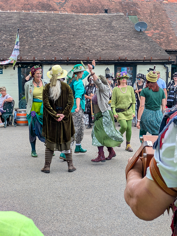 Asum Gras Molly in various shades of green costume dancing in a close knit circle