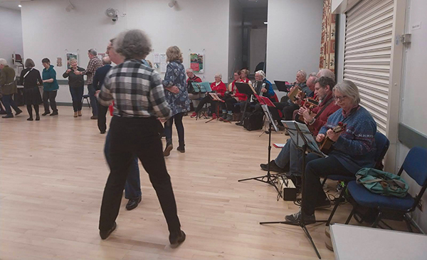 musicians from combined bands seated at the edge of the hall playing for a folk dance