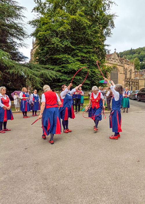 view of dancers dancing with hoops against a background of Malvern Priory and the Malvern Hills in the distance