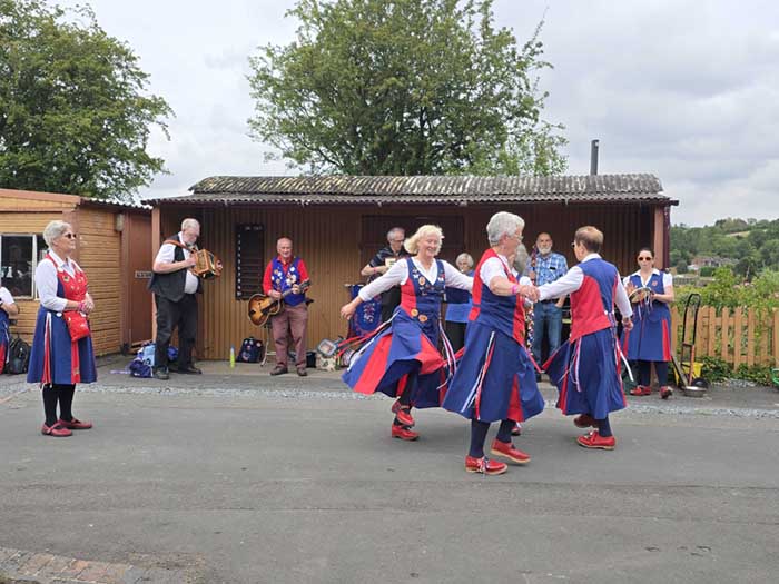 Musicians playing under the awning of a shed in case of rain and dancers dancing in the station yard