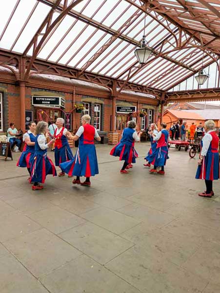 2 groups of Butterfly Dancers dancing in the Kidderminster station Concourse under the decorative cast iron and glass Victorian roof