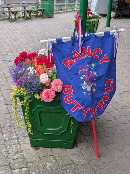 Nancy Butterfly's new pennant leaning against an attractive tub of colourful flowers outside Highley Engine House