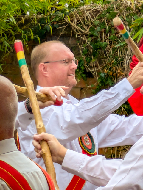 View of White Hart dancer amongst several white clad arms and wooden sticks during a dance