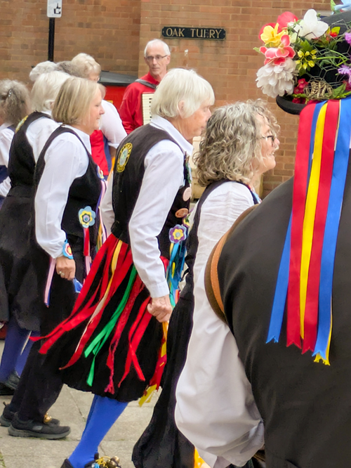 Row of Ladies from the Flowers of Ilmington side in black and white costumes decorated with colourful badges and ribbons, during a dance