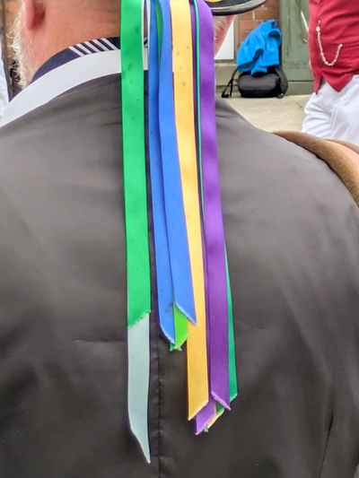 Close-up view of thye back of a Flowers of Ilmington musician with a stream of colourful ribbons falling down from his hat