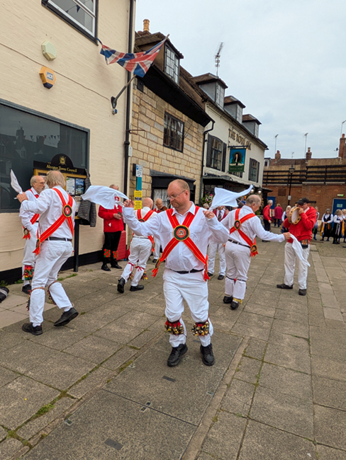 White Hart Morris in their traditional white Cotswold attire dancing on the pavement in front of the Royal Oak pub in Alcester. Their white hankies are conspicuous.